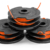 Bild på ett 3-pack Husqvarna Spole med A15B lina, som visar svarta spolar med orange trimningslina utstående. Denna produkt är avsedd för effektiv och jämn trimning och är kompatibel med Husqvarna 110iL.
