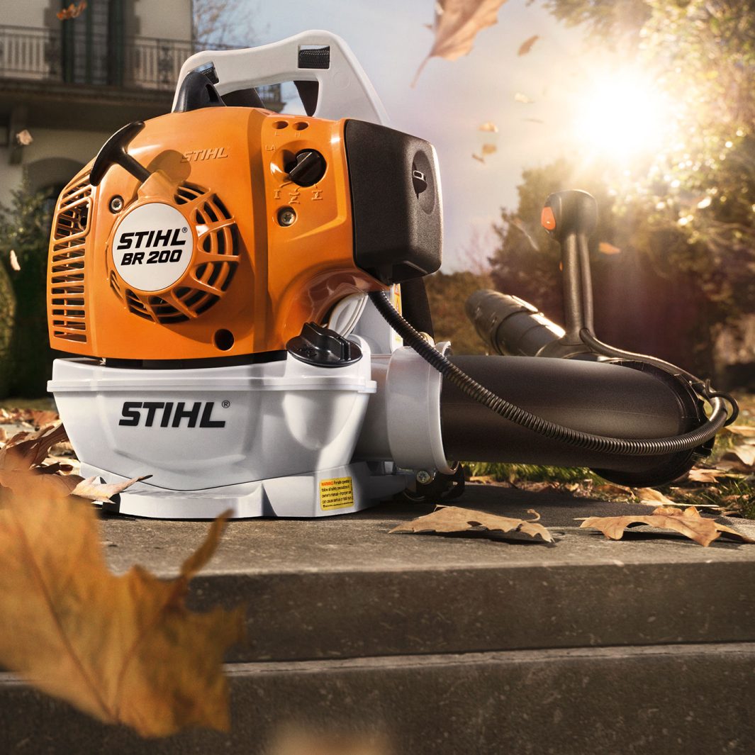 Stihl BR 200 Lövblås placerad i en trädgård med fallande löv, framhävande maskinens detaljer och design i solnedgångsljus